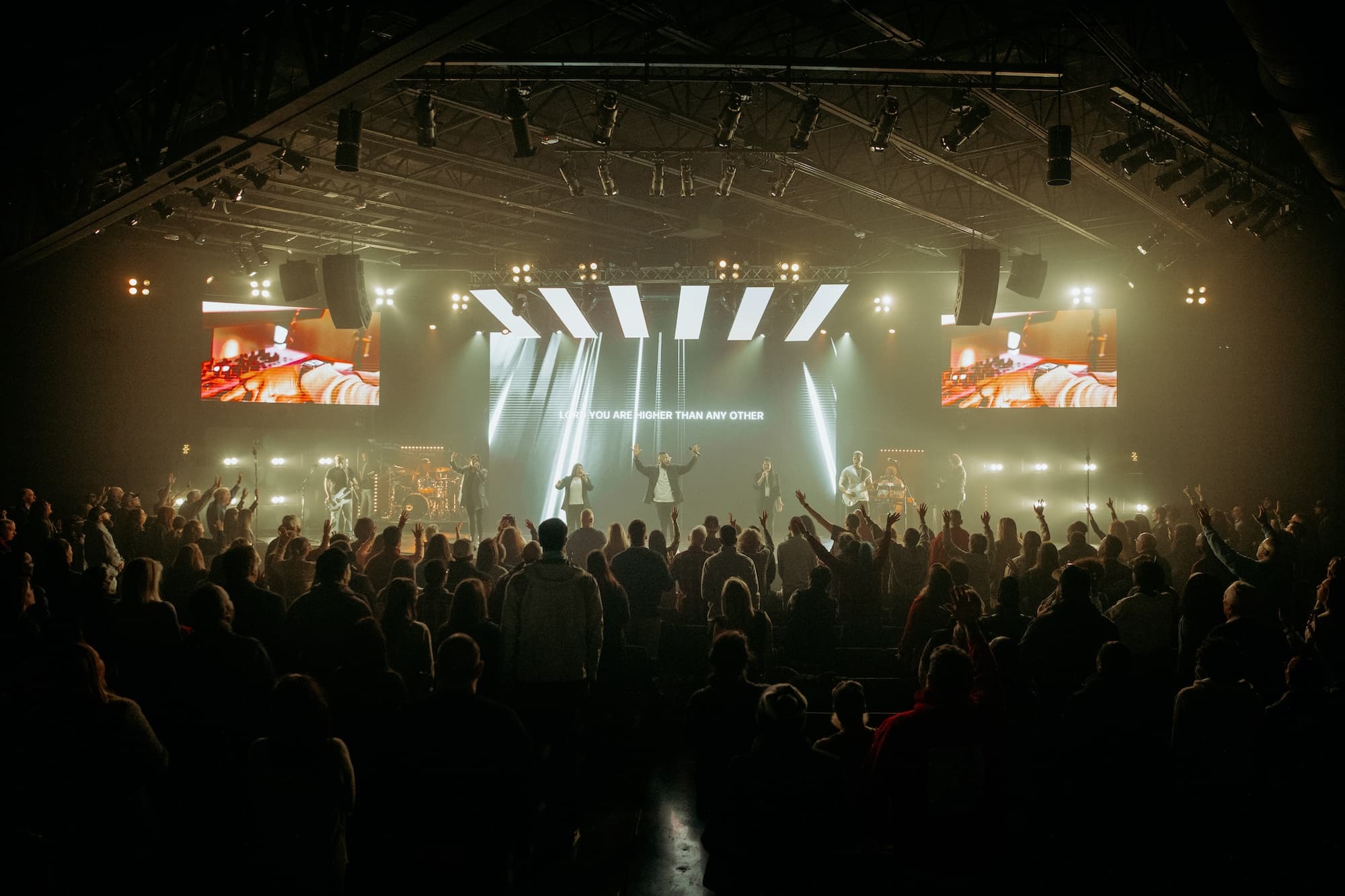 A packed Waters Church auditorium during worship, with a live band and bright stage lights